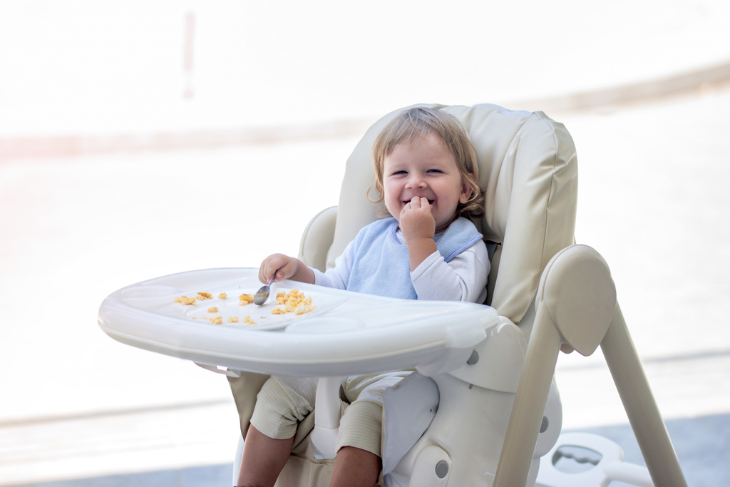 Happy baby boy eating breakfast in high chair.