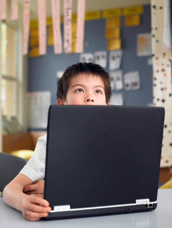 Thoughtful Boy Sitting By Laptop In Classroom