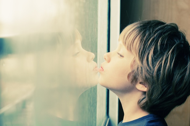 Cute 6 years old boy looking through the window
