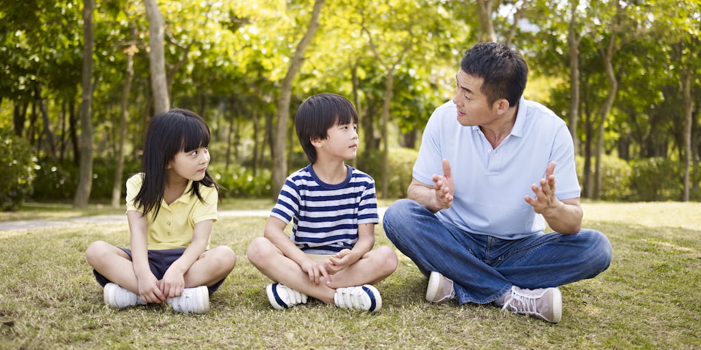 asian father and children talking in park